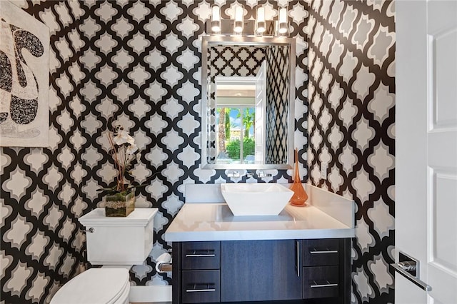 bathroom with toilet, wallpapered walls, and vanity