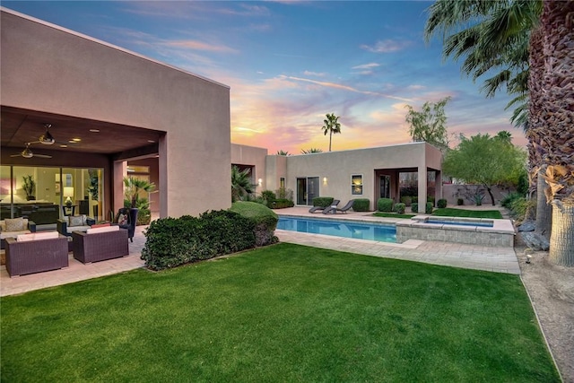 pool at dusk featuring a pool with connected hot tub, a lawn, a patio area, and an outdoor living space