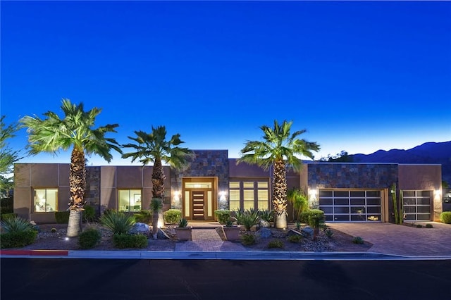 contemporary home with a garage, decorative driveway, a mountain view, and stucco siding