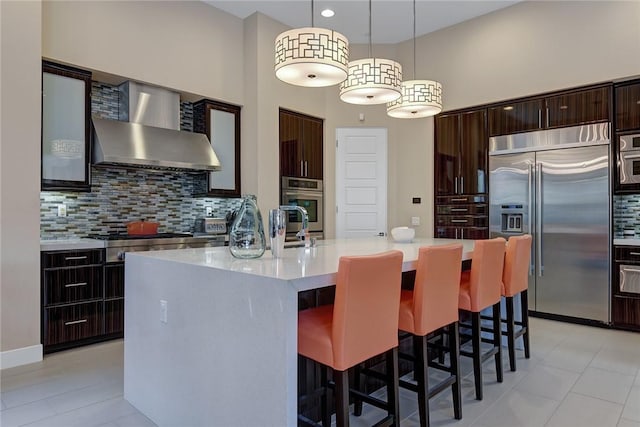 kitchen with appliances with stainless steel finishes, light countertops, wall chimney range hood, and a breakfast bar area