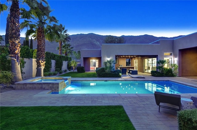 view of pool featuring a pool with connected hot tub, a mountain view, a lawn, and a patio