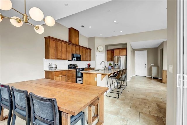 kitchen featuring a breakfast bar area, light countertops, appliances with stainless steel finishes, brown cabinetry, and a kitchen island with sink