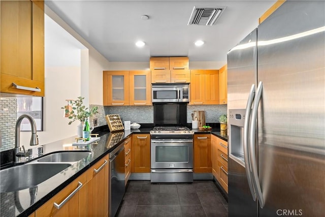 kitchen featuring stainless steel appliances, a sink, visible vents, dark stone countertops, and glass insert cabinets