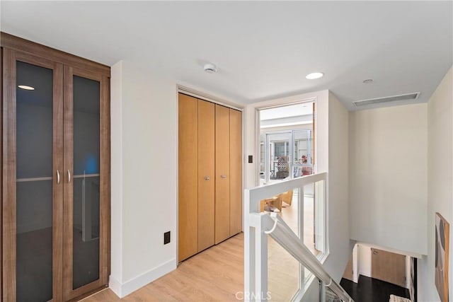 corridor with light wood-type flooring, visible vents, and an upstairs landing