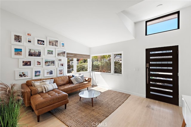 living area with light wood-type flooring, baseboards, and vaulted ceiling