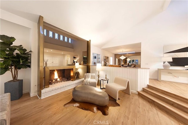 living area featuring baseboards, high vaulted ceiling, a brick fireplace, and light wood-style floors