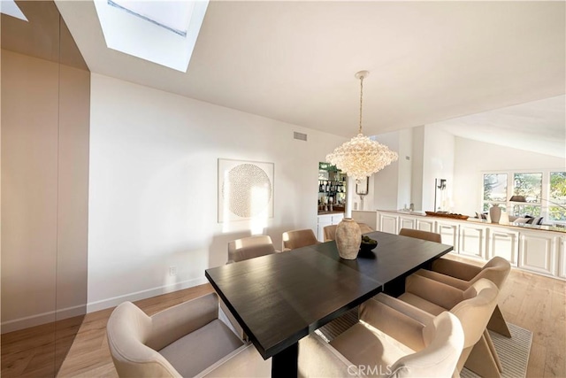 dining room featuring visible vents, baseboards, lofted ceiling with skylight, light wood-style flooring, and an inviting chandelier