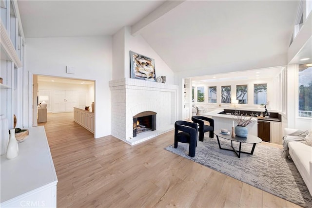 living room with light wood finished floors, visible vents, beamed ceiling, a fireplace, and high vaulted ceiling