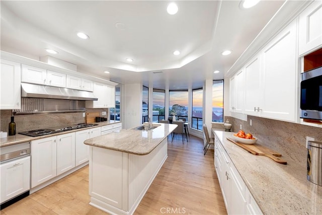 11 Montpellier, Newport Beach, CA 92660 - kitchen with under cabinet range hood, black electric cooktop, tasteful backsplash, a kitchen island, and white cabinetry