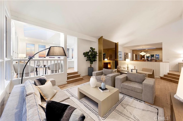 living room featuring stairs, vaulted ceiling, light wood-style flooring, and baseboards