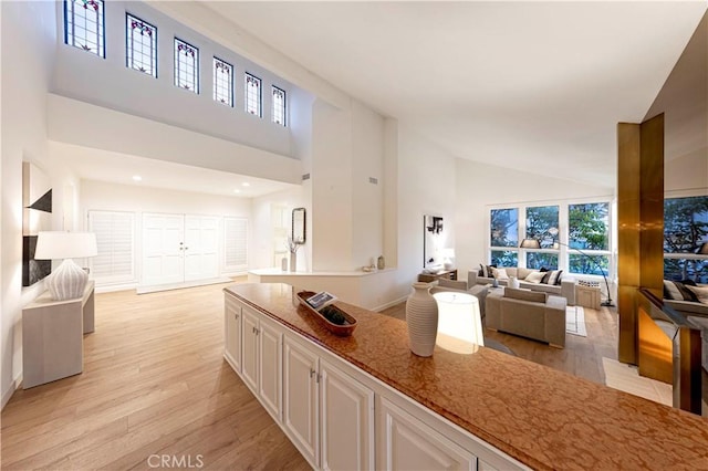 kitchen with stone countertops, open floor plan, light wood-type flooring, white cabinetry, and high vaulted ceiling