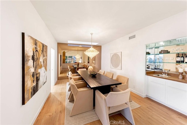 dining space featuring a chandelier, visible vents, baseboards, light wood-type flooring, and wet bar