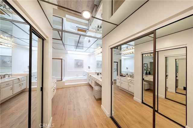 full bathroom featuring a bath, two vanities, wood finished floors, a shower stall, and a sink