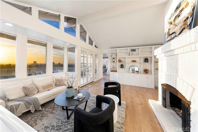 living room with high vaulted ceiling, light wood-style flooring, french doors, a brick fireplace, and beam ceiling