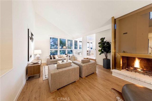 living room featuring light wood-style flooring, a fireplace, high vaulted ceiling, and baseboards