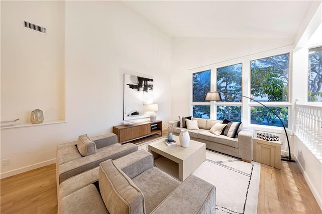 living room with high vaulted ceiling, baseboards, visible vents, and light wood finished floors