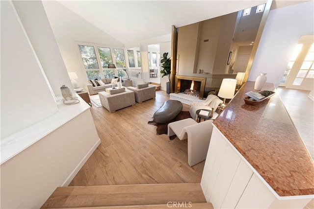 living room featuring light wood finished floors, a lit fireplace, and high vaulted ceiling