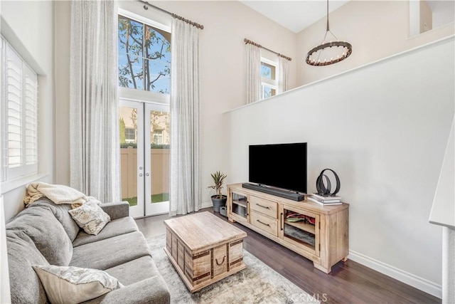 living area featuring dark wood-type flooring, french doors, a towering ceiling, and baseboards