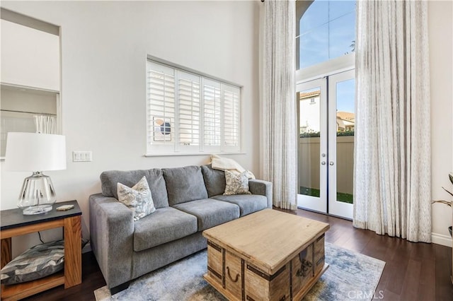 living area featuring dark wood-style flooring, a healthy amount of sunlight, a towering ceiling, and french doors