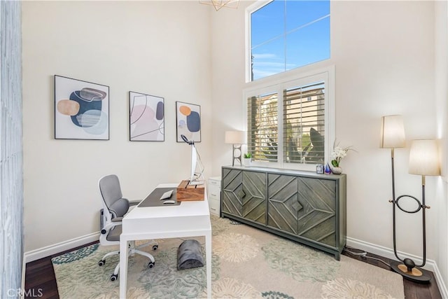 home office with a high ceiling, wood finished floors, and baseboards