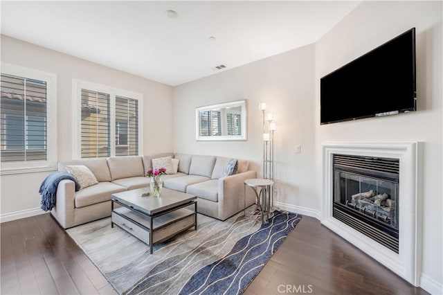 living area featuring baseboards, visible vents, wood finished floors, and a glass covered fireplace