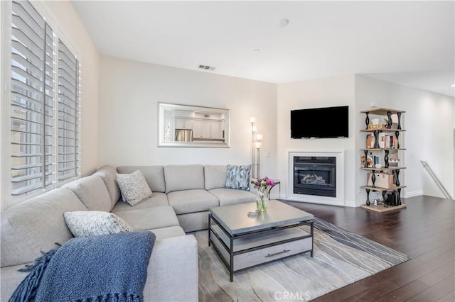 living room featuring a glass covered fireplace, wood finished floors, visible vents, and baseboards