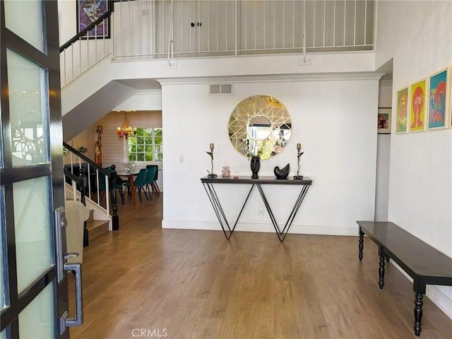 foyer entrance featuring visible vents, a towering ceiling, stairway, wood finished floors, and a chandelier