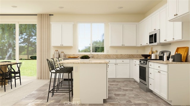 kitchen featuring a center island, white cabinets, stainless steel electric range, light stone countertops, and a kitchen bar