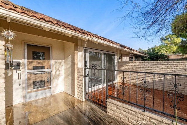 view of exterior entry with a tiled roof, a patio, fence, and stucco siding