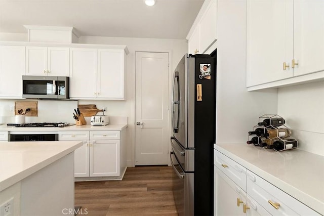 kitchen with appliances with stainless steel finishes, white cabinets, light countertops, and wood finished floors