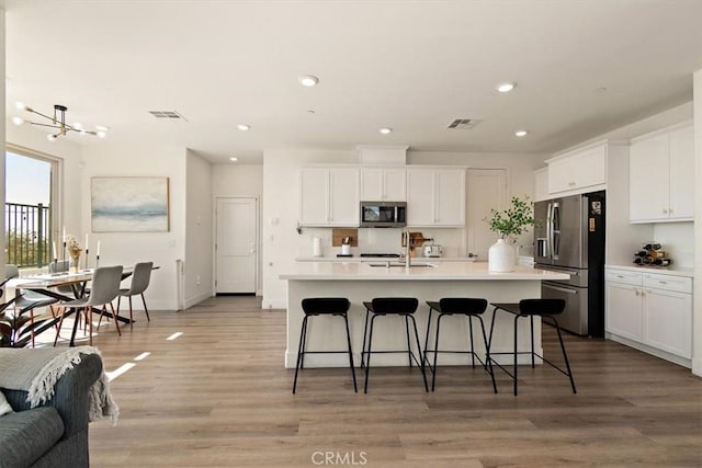 kitchen featuring stainless steel appliances, light countertops, a center island with sink, and white cabinets