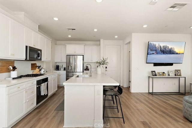 kitchen featuring stainless steel appliances, a sink, white cabinetry, light countertops, and a center island with sink