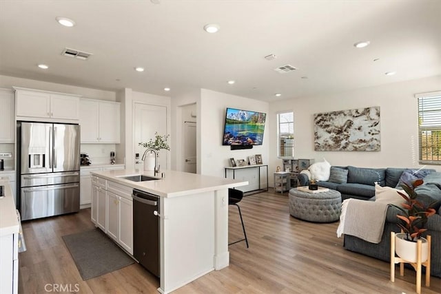 kitchen with stainless steel fridge, a center island with sink, open floor plan, light countertops, and a sink