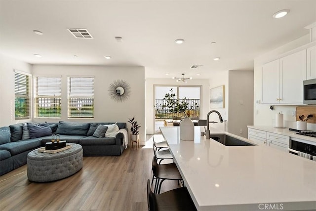 kitchen featuring light countertops, open floor plan, white cabinetry, a sink, and a large island with sink