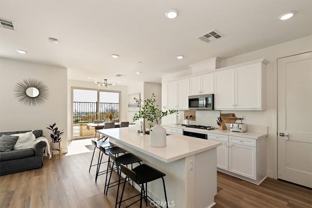 kitchen featuring stainless steel appliances, light countertops, visible vents, white cabinets, and an island with sink