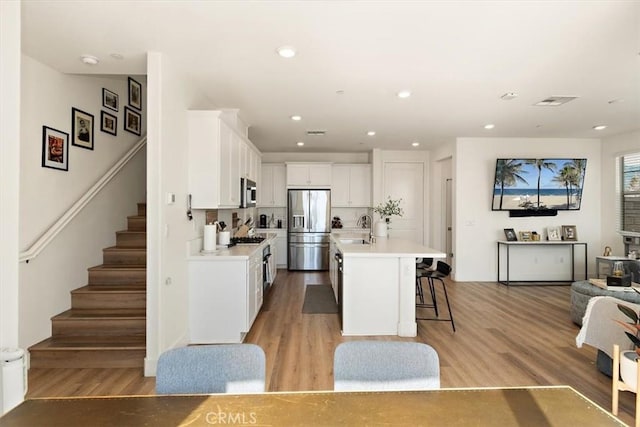 kitchen with stainless steel appliances, white cabinets, open floor plan, light countertops, and a center island with sink