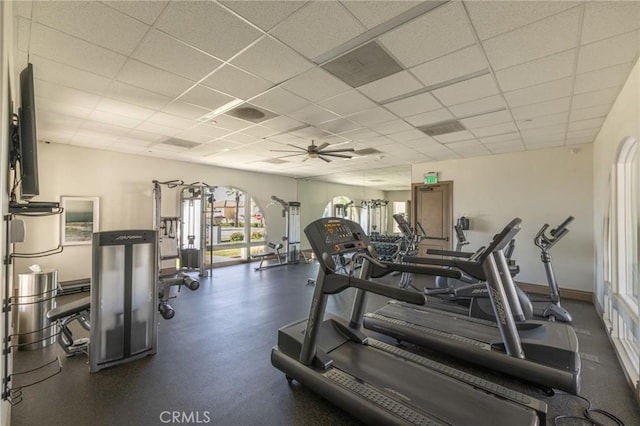 exercise room with baseboards, ceiling fan, arched walkways, and a drop ceiling