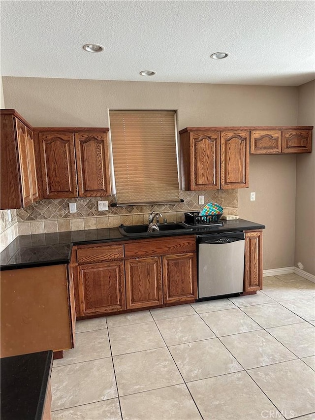 kitchen with brown cabinetry, dark countertops, a sink, and stainless steel dishwasher