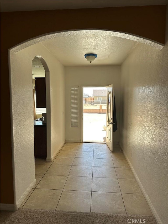 doorway featuring light tile patterned floors, baseboards, arched walkways, a textured wall, and a textured ceiling