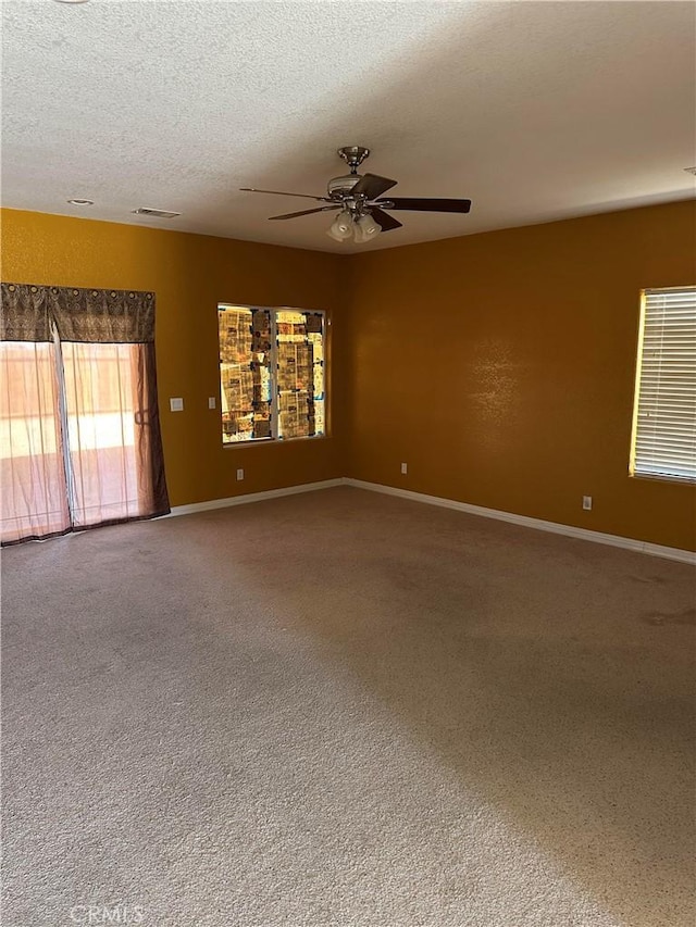 carpeted spare room featuring baseboards, visible vents, a ceiling fan, and a textured ceiling