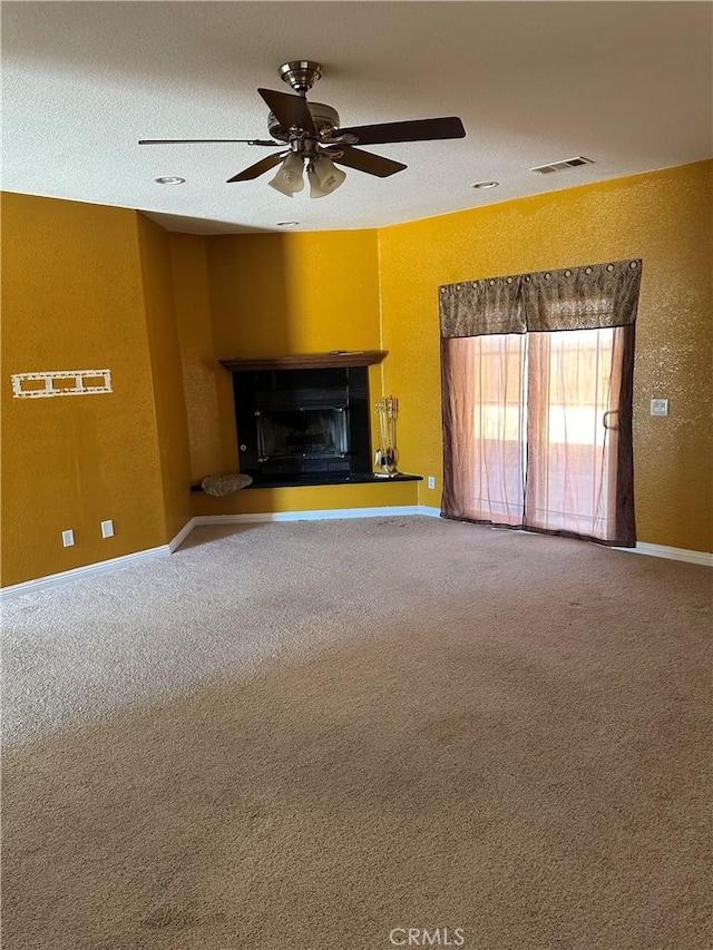 unfurnished living room with a fireplace with raised hearth, ceiling fan, visible vents, baseboards, and carpet