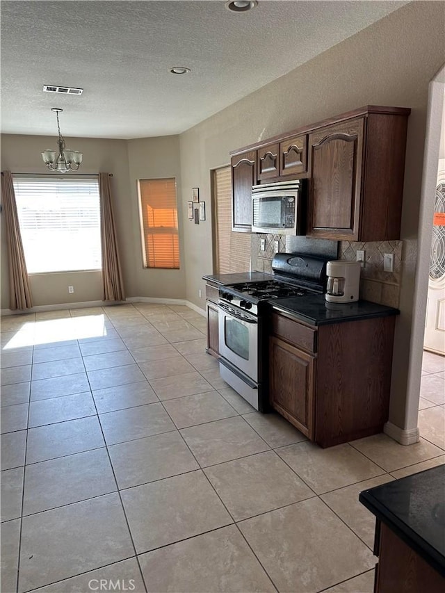 kitchen featuring light tile patterned floors, stainless steel appliances, visible vents, tasteful backsplash, and dark countertops