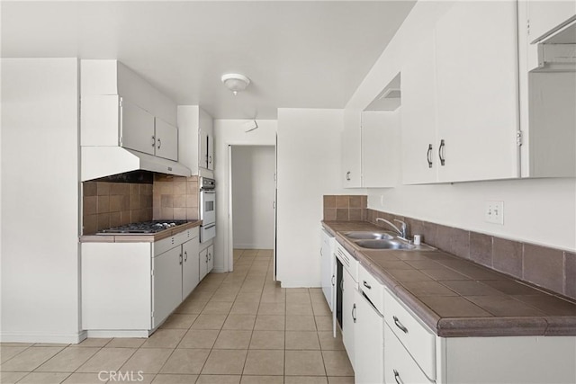 kitchen featuring tile counters, white cabinetry, a sink, and under cabinet range hood