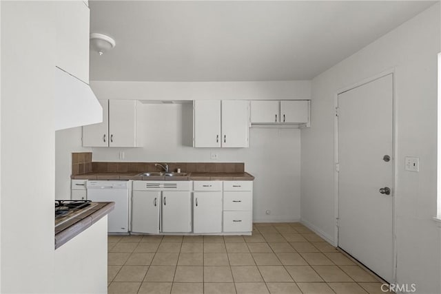 kitchen with dark countertops, white dishwasher, white cabinets, and a sink