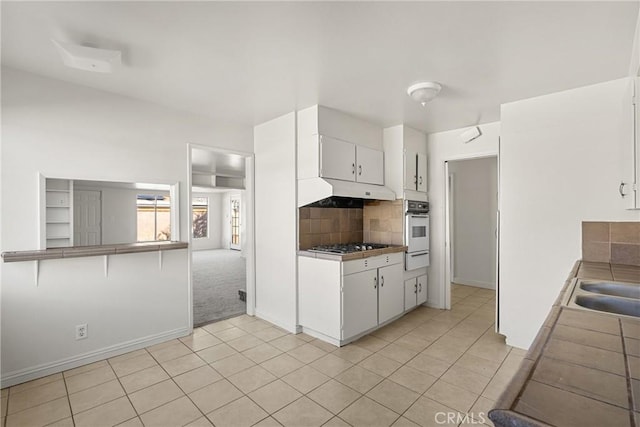 kitchen featuring white oven, backsplash, white cabinets, and under cabinet range hood