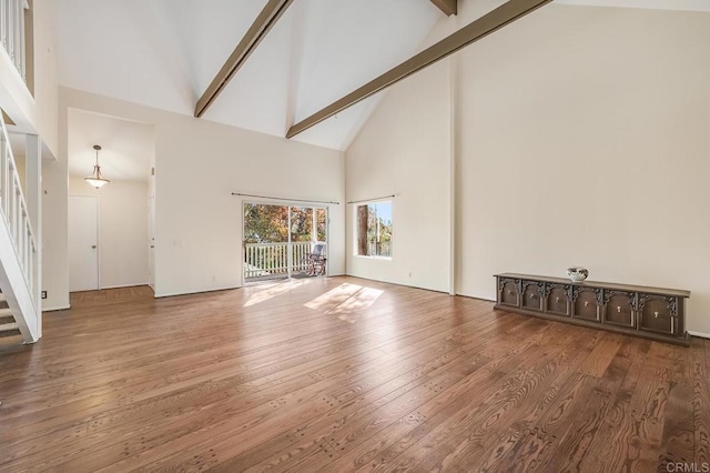 unfurnished living room with wood finished floors, high vaulted ceiling, beam ceiling, and stairs