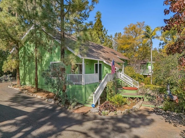 rustic home with stairway, a shingled roof, and covered porch