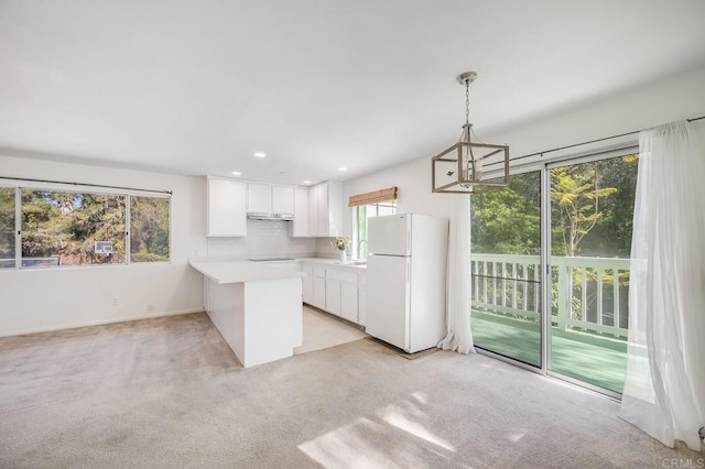 kitchen with hanging light fixtures, white cabinets, light countertops, freestanding refrigerator, and a peninsula