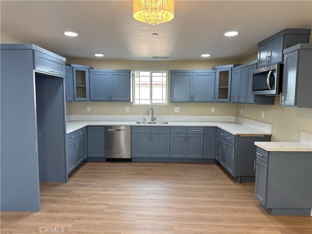 kitchen with stainless steel appliances, light wood-style floors, glass insert cabinets, and a sink