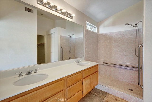 bathroom featuring double vanity, tiled shower, a sink, and visible vents